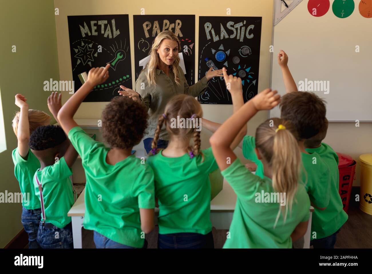 Professeur d'école féminine pointant vers une affiche de recyclage avec un groupe d'écoliers qui élèvent leur ha Banque D'Images