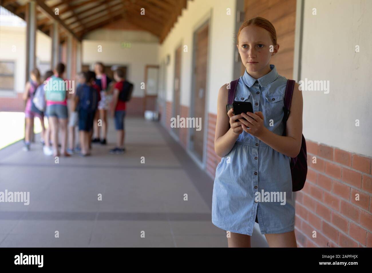 une écolière se tenant dans la cour de l'école primaire à l'aide d'un smartphone Banque D'Images