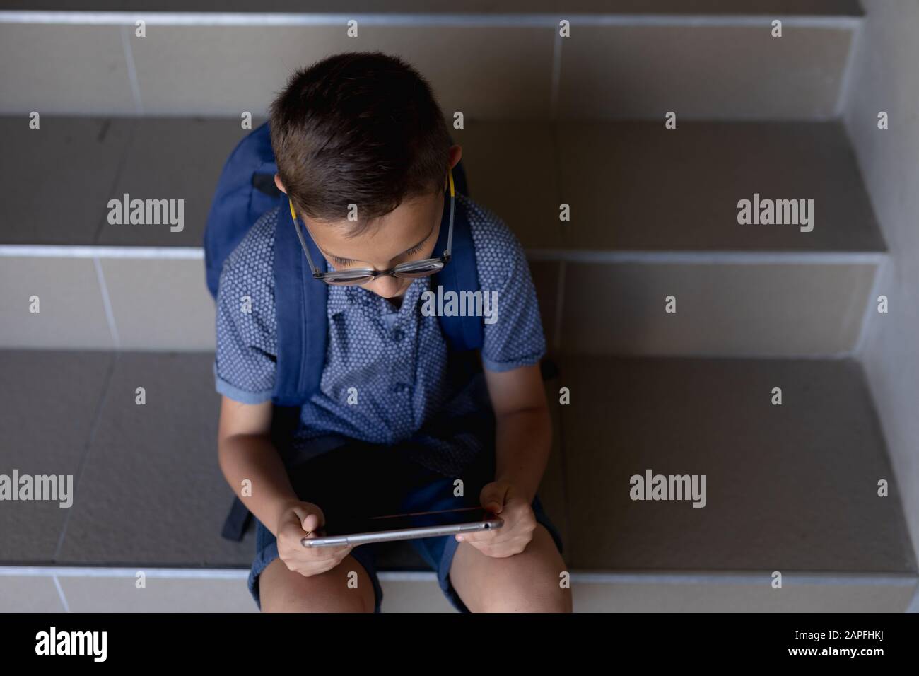 Un écolier assis sur un pas à côté d'un mur dans la cour de l'école primaire à l'aide d'un ordinateur tablette Banque D'Images