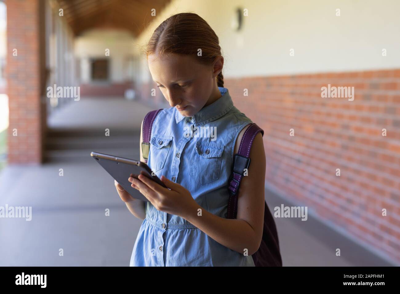 Une écolière se tenant dans la cour de l'école primaire à l'aide d'un ordinateur tablette Banque D'Images