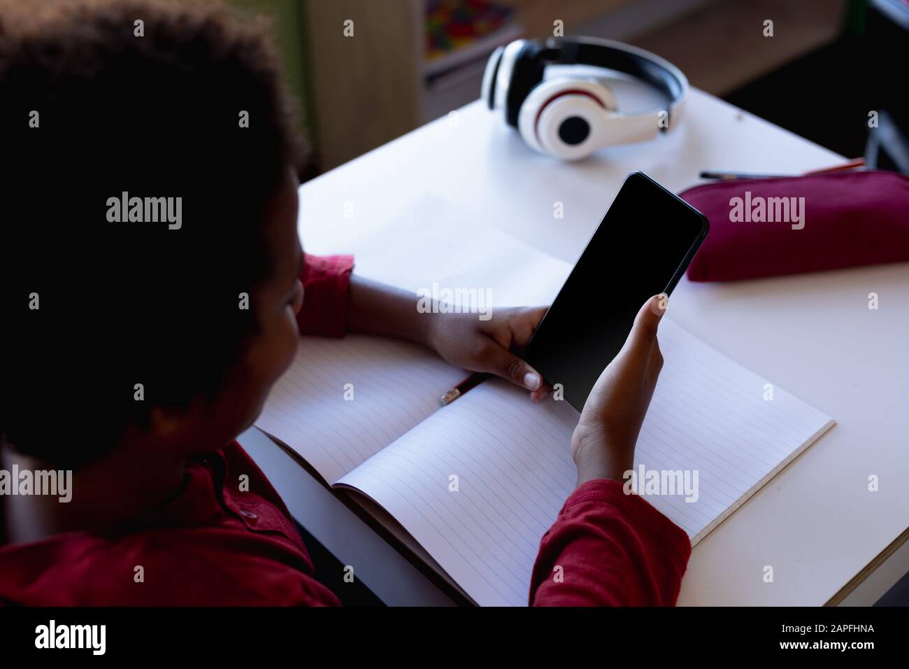 Un écolier assis à un bureau à l'aide d'un smartphone dans une salle de classe de l'école primaire Banque D'Images