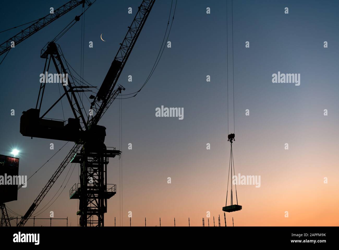 Silhouette de grues de tour de construction levage de matériaux de construction au coucher du soleil - grue industrielle levage de béton au développement de gratte-ciel de ville - immobilier, développement et bloc d'appartements Banque D'Images