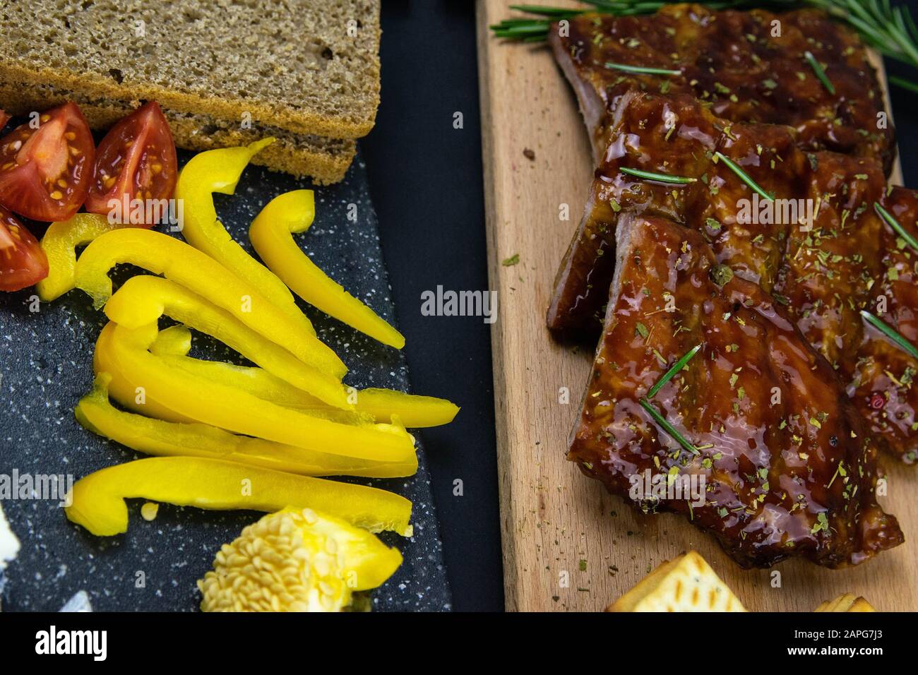 Côtes sous sauce au miel sur une planche en bois à côté des tomates, du pain et du papier cloche. Vues de dessus Banque D'Images