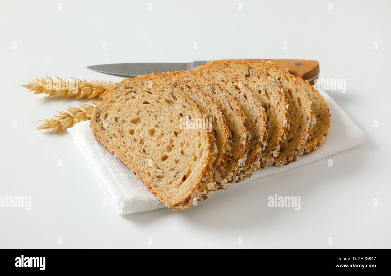 Pain en tranches de pain de grain entier sur la serviette blanche, les oreilles de blé et le couteau de cuisine à côté Banque D'Images