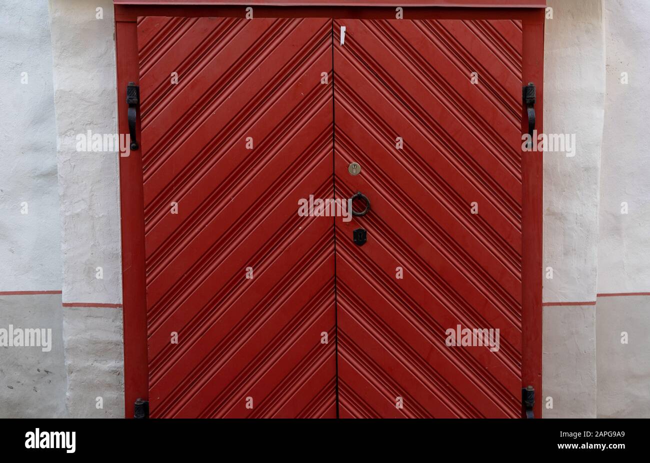 Grande porte en bois rouge avec poignées et charnières forgées noires dans un bâtiment ancien. Banque D'Images