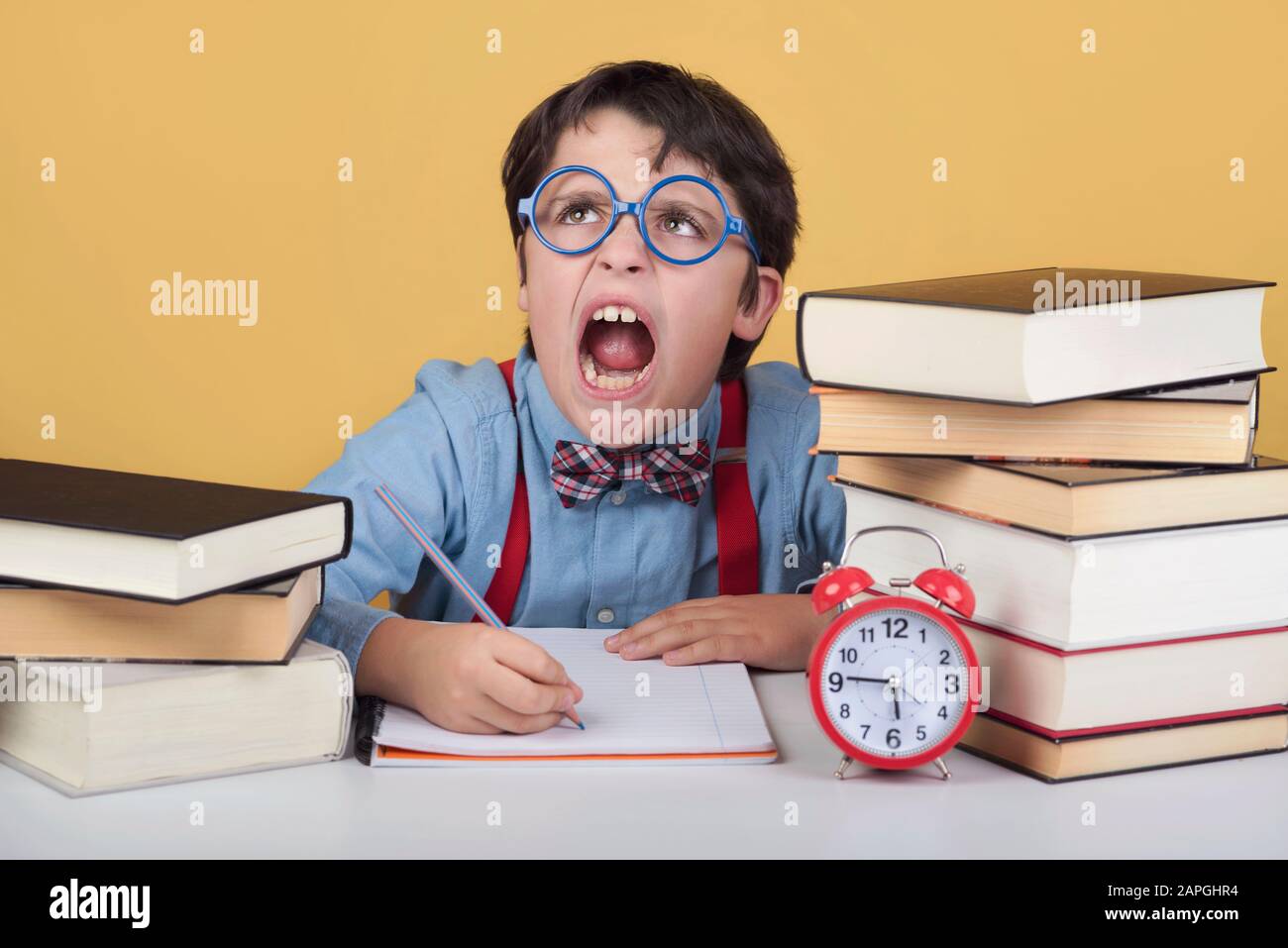 enfant en colère avec des livres sur une table sur fond jaune Banque D'Images