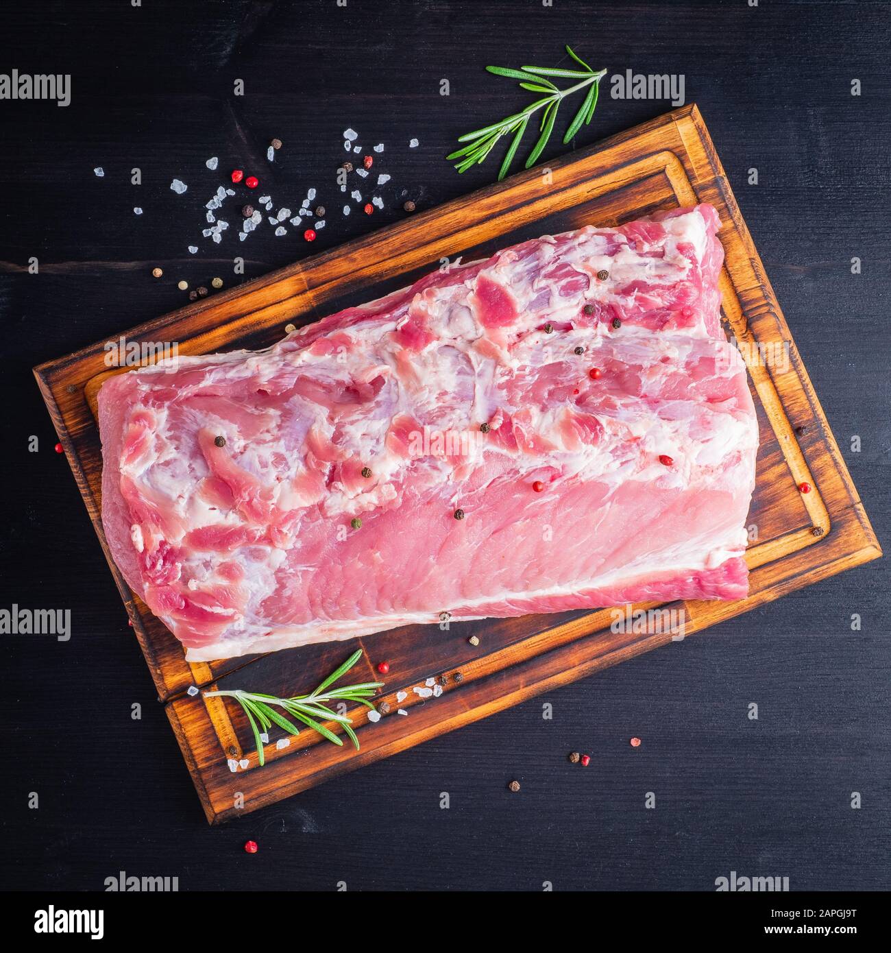 Gros morceau entier de viande de porc avec assaisonnement sur hacher planche sur fond noir Banque D'Images