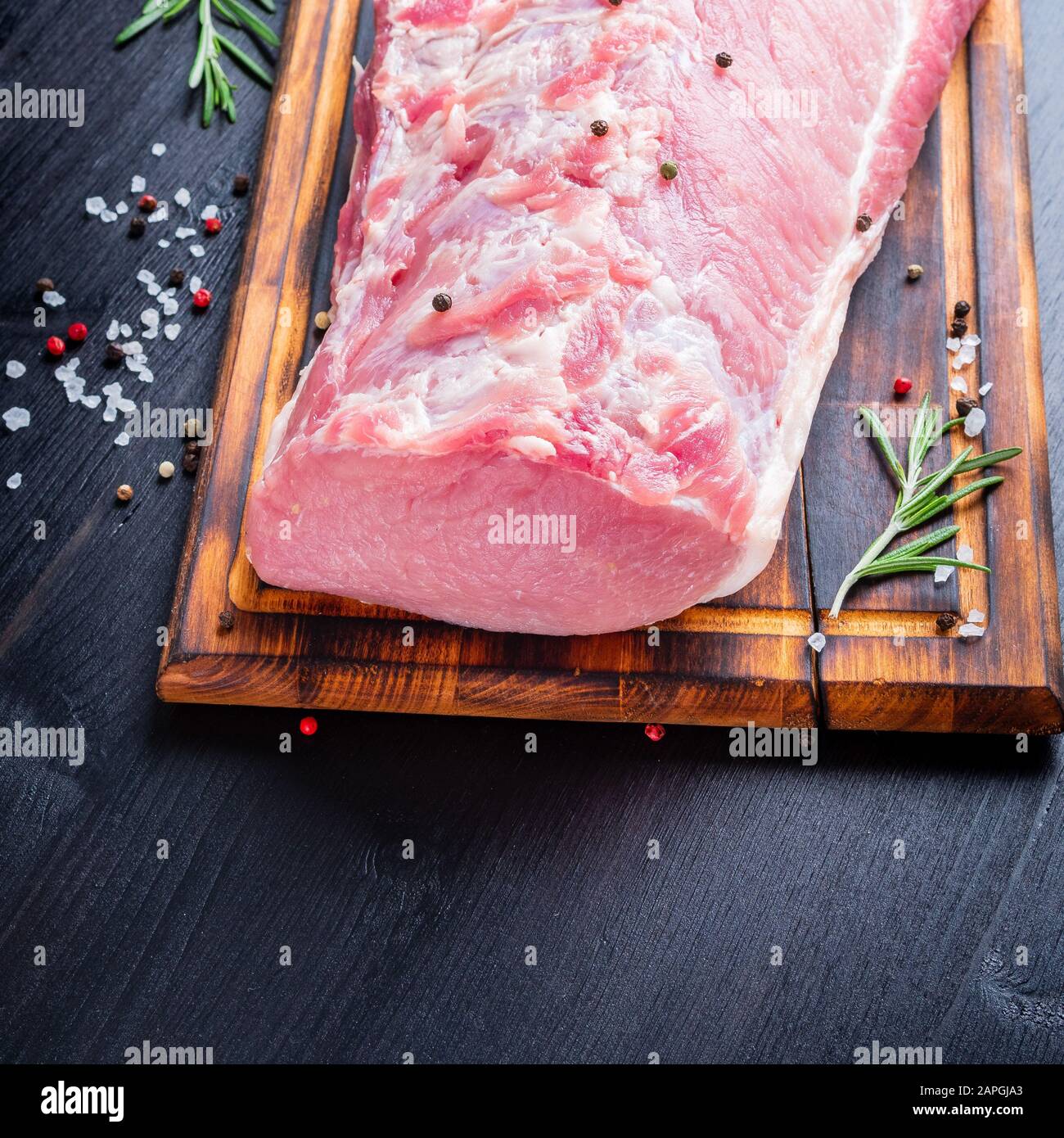 Gros morceau entier de viande de porc avec assaisonnement sur hacher planche sur fond noir Banque D'Images