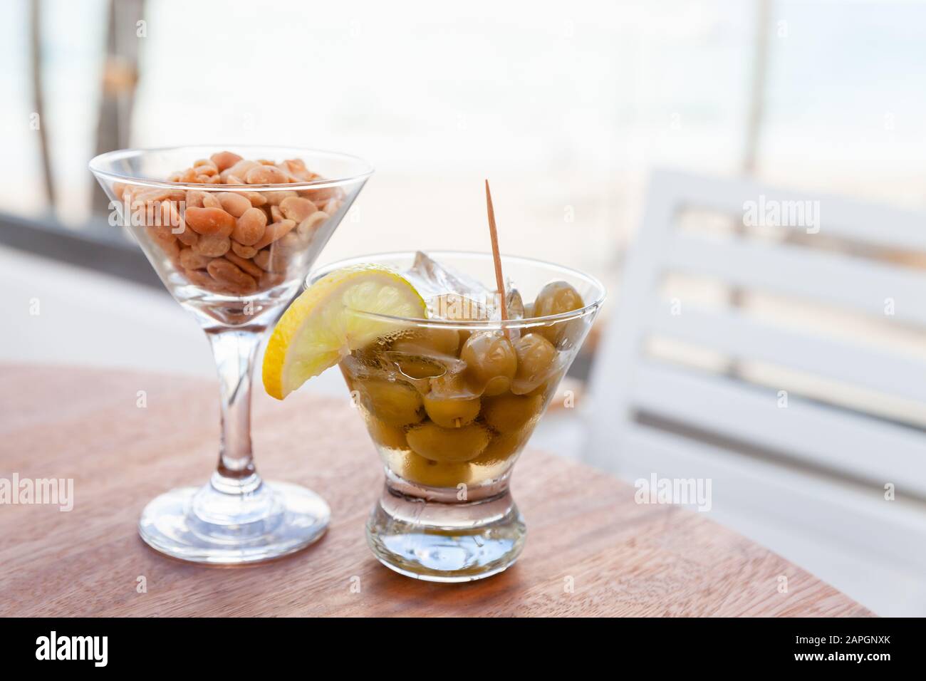 Les olives vertes au citron et à la glace et les arachides dans les verres sont sur une table ronde en bois, apéritif gratuit dans un bar, photo avec un foyer sélectif Banque D'Images