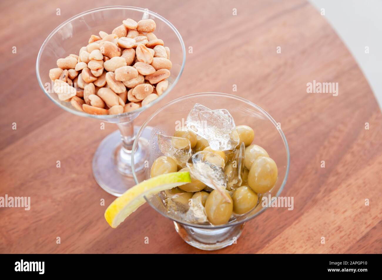 Les olives vertes au citron et à la glace et les arachides dans les verres se tiennent sur une table ronde en bois, apéritif gratuit dans un bar, vue sur le dessus Banque D'Images
