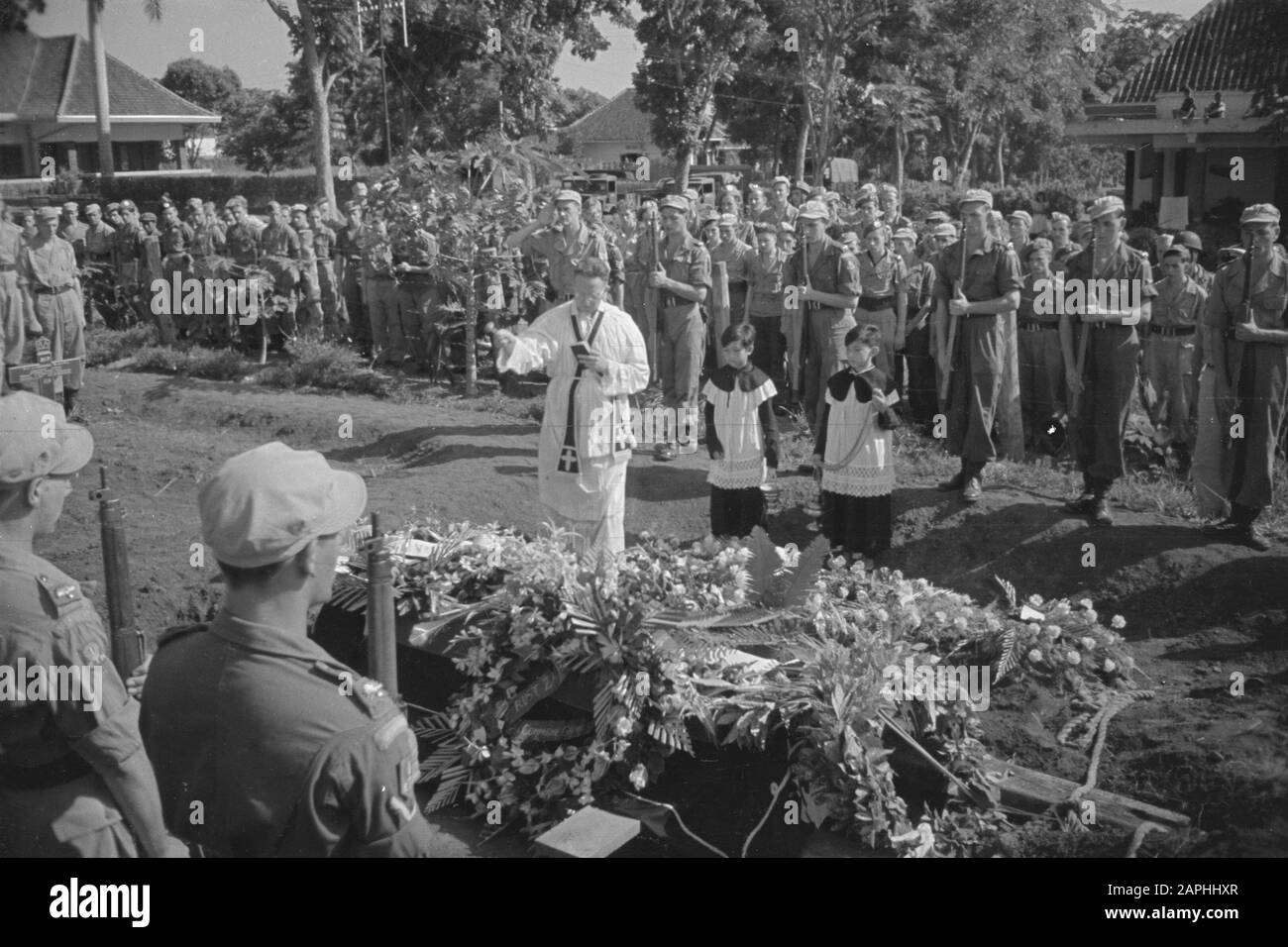 Action soins de plein air Description: [Le cercueil avec les restes d'un soldat tombé couvert de fleurs près de la tombe est béni par un prêtre catholique romain. Près de lui 2 officiers d'autel] Date: 20 juillet 1947 lieu: Indonésie, Java, Pays-Bas Antilles orientales Banque D'Images