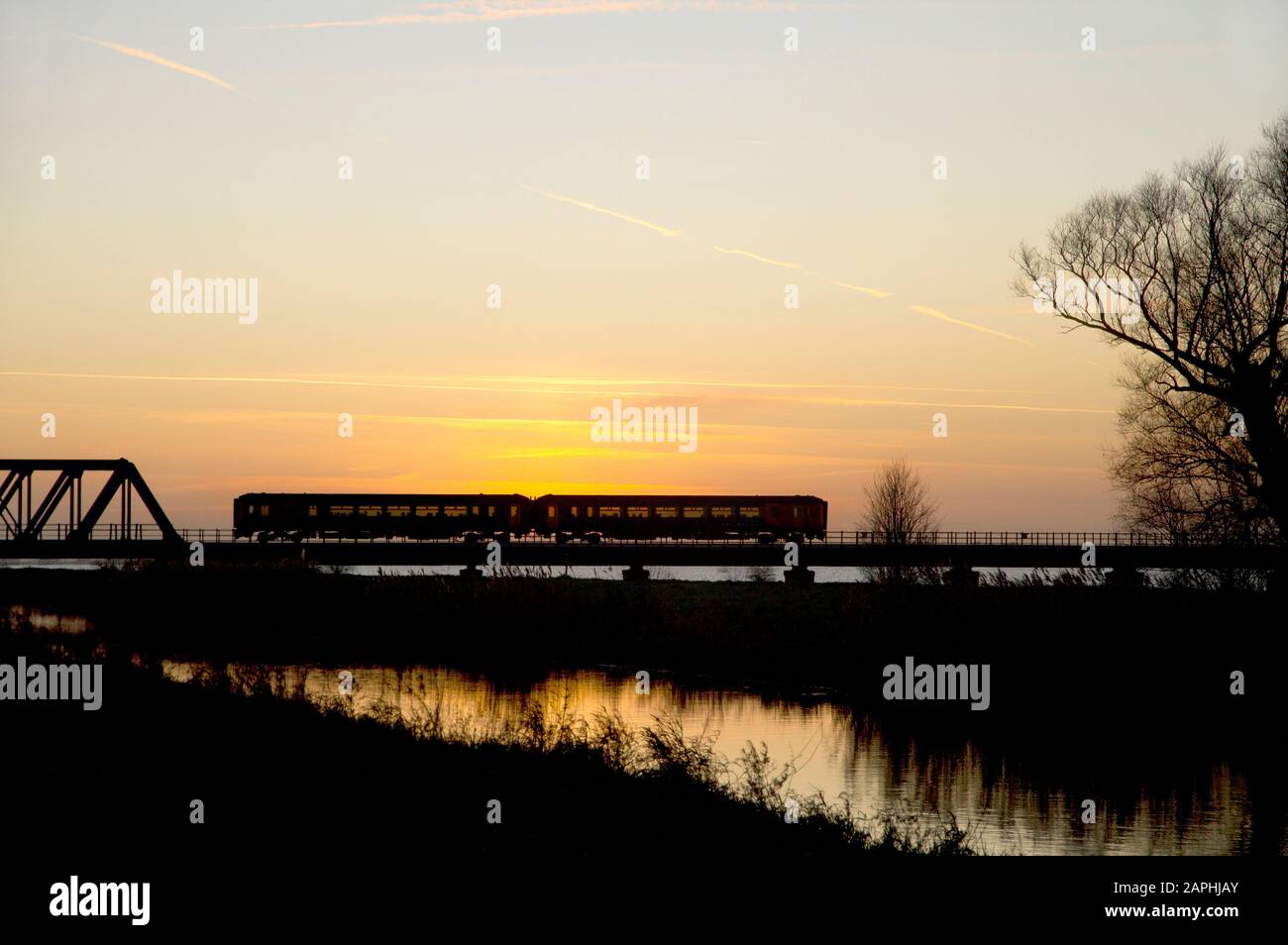 Une unité multiple diesel de classe 156 qui travaille un service ferroviaire East Midland traverse Les Cent Pieds Lavés près de Welney/Pymoor au coucher du soleil. Banque D'Images