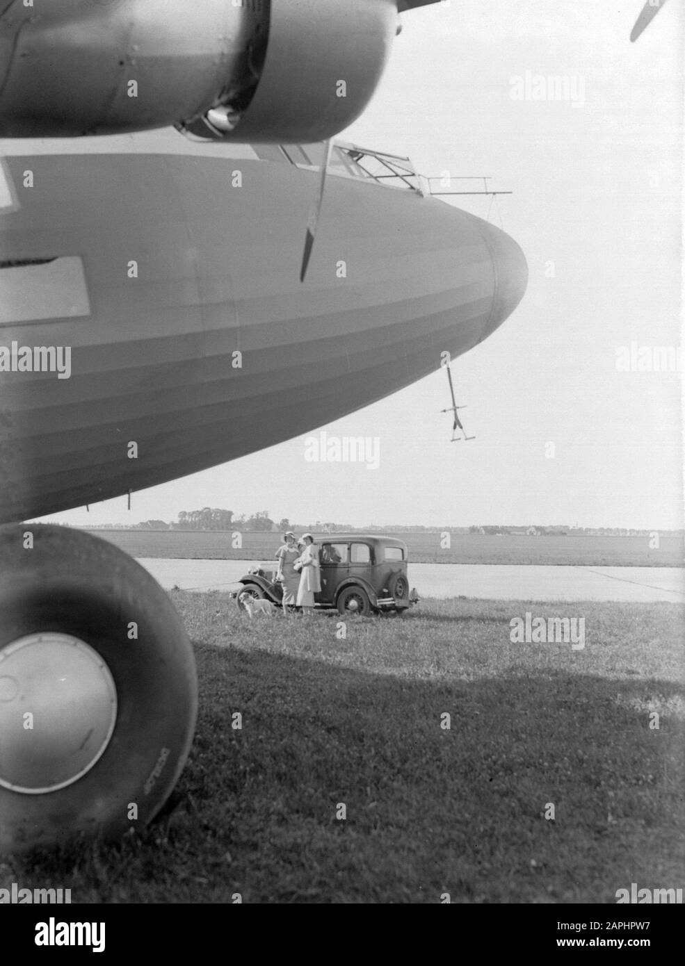 Anthony Fokker Description: Le nez de l'avion à quatre moteurs le Fokker F XXXVI à l'aéroport de Schiphol en arrière-plan deux dames avec un pouxterrier penchant contre l'automobile d'Austin. Date : le 27 août 1934 lieu : Noord-Holland, Schiphol mots clés : voitures, avions, aéroports Banque D'Images