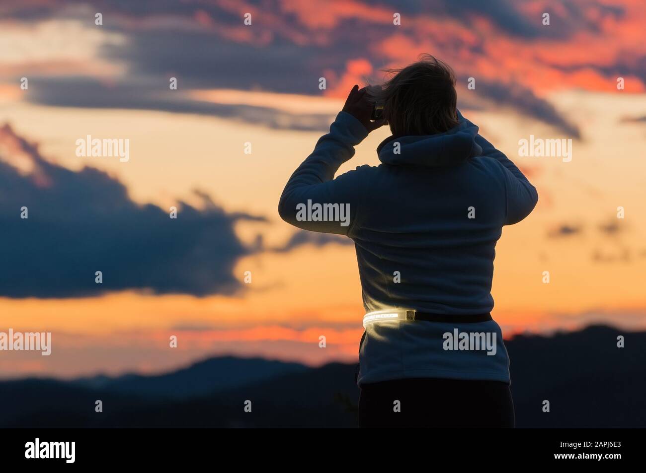 Randonneur féminin prenant des photos du magnifique ciel au coucher du soleil avec smartphone. Concepts de randonnée, d'optimisme, de météo et d'environnement Banque D'Images