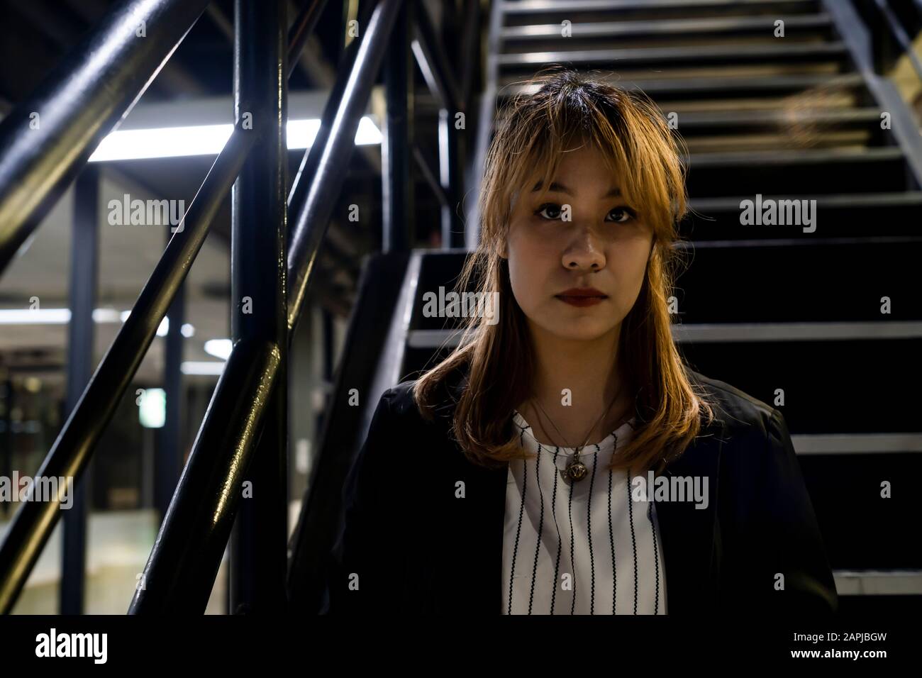 Gros plan moyen de femme cheveux blonde en vêtements noir et blanc assis sur l'escalier avec main courante en métal regardant l'appareil photo. Banque D'Images