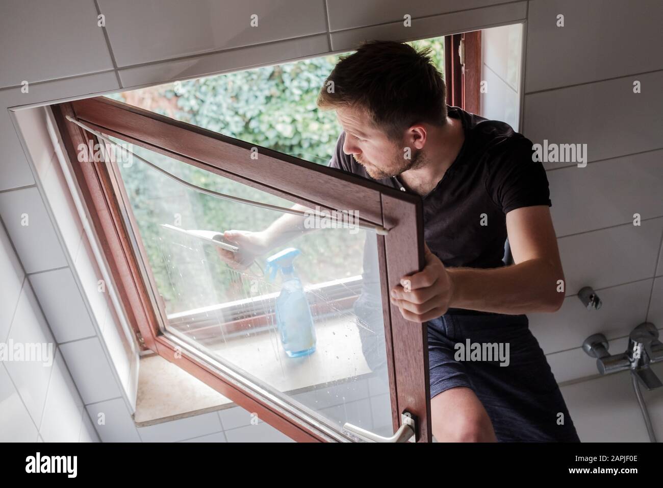 Un homme caucasien lave une fenêtre dans une maison à l'aide d'un grattoir Banque D'Images