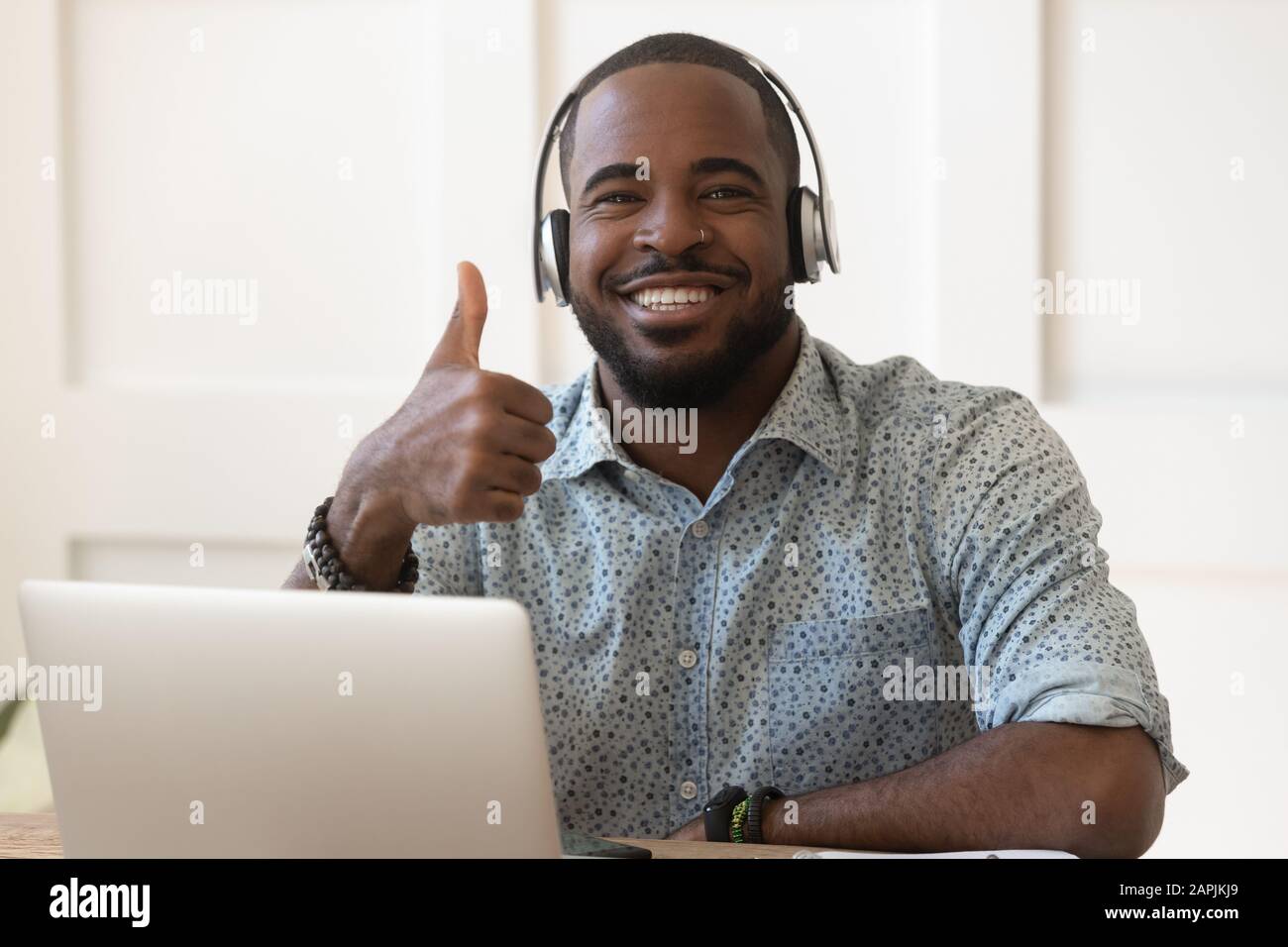 Un gars africain dans un casque assis près de l'ordinateur montrant des pouces vers le haut Banque D'Images