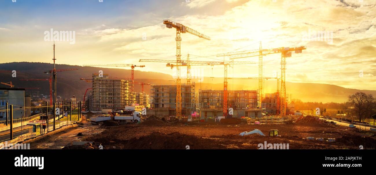 Grand chantier de construction comprenant plusieurs grues travaillant sur un complexe de construction, illuminées par la lumière chaude de l'or Banque D'Images