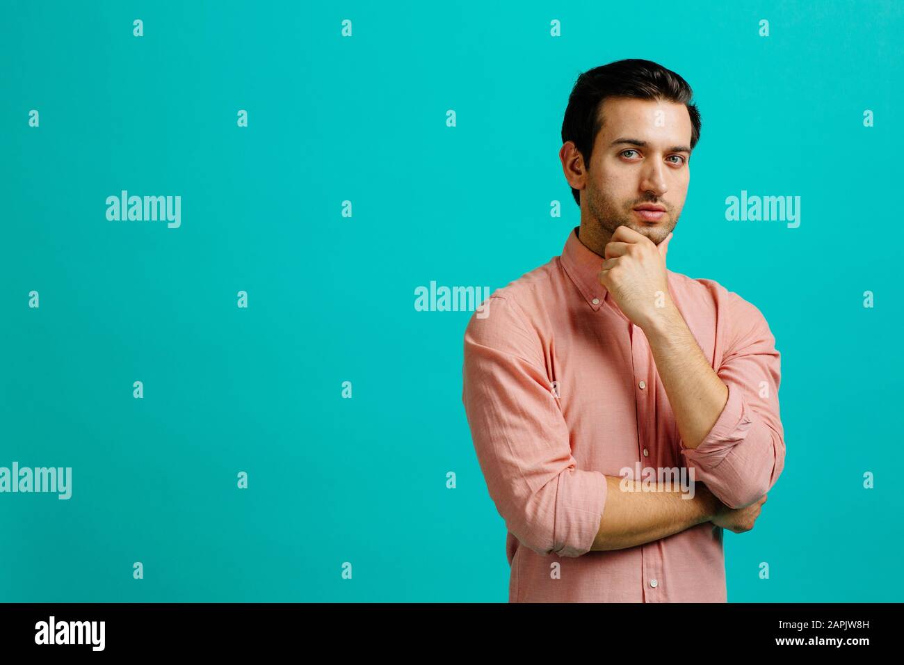 Portrait d'un jeune homme adulte main sur le menton, bras croisés, isolé sur fond bleu de studio Banque D'Images