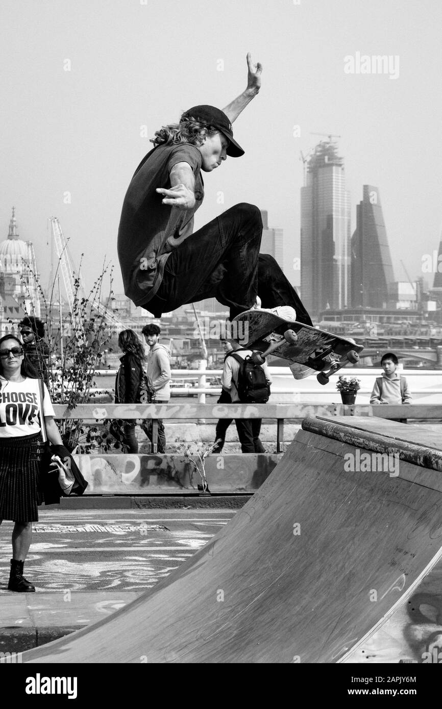 Photographie de rue en noir et blanc à Londres : le skateboarder effectue une manœuvre sur toile de fond de la City de Londres. Banque D'Images