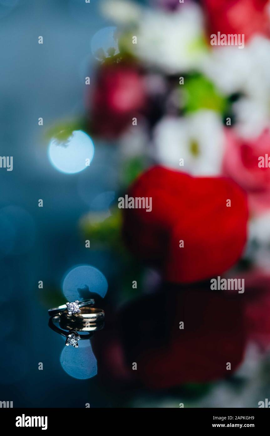 Deux anneaux d'engagement et une boîte en velours rouge en forme de coeur sur fond avec des lumières et des fleurs bokeh. Saint-Valentin. Cadeaux pour femme sur Valentin Banque D'Images