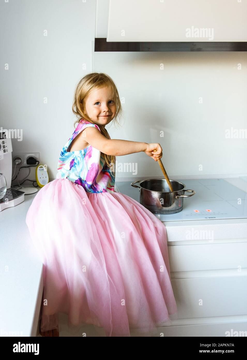 Petite fille en robe élégante assise sur une table dans la cuisine Banque D'Images