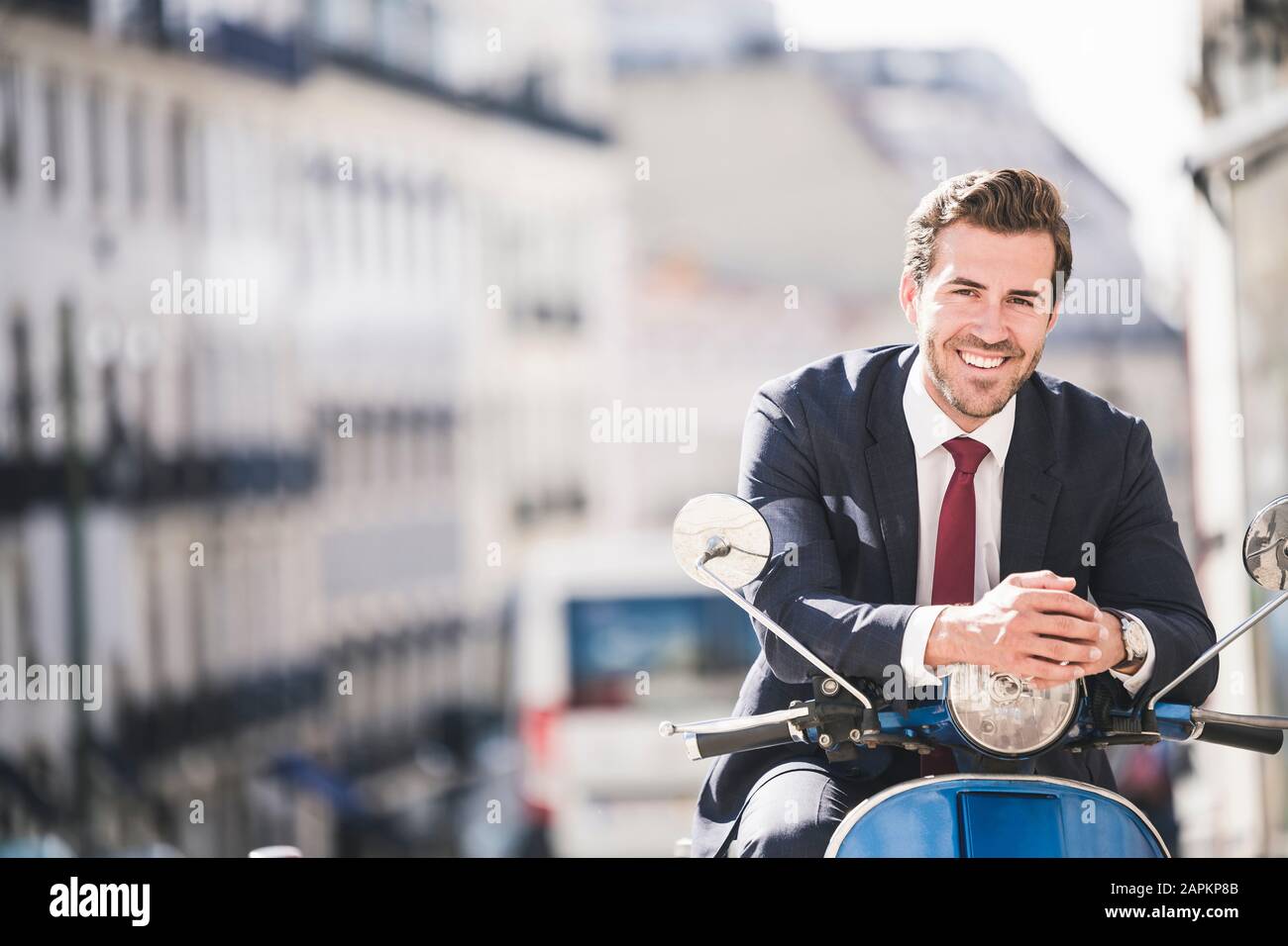 Portrait de jeune homme d'affaires souriant sur scooter automobile dans la ville, Lisbonne, Portugal Banque D'Images