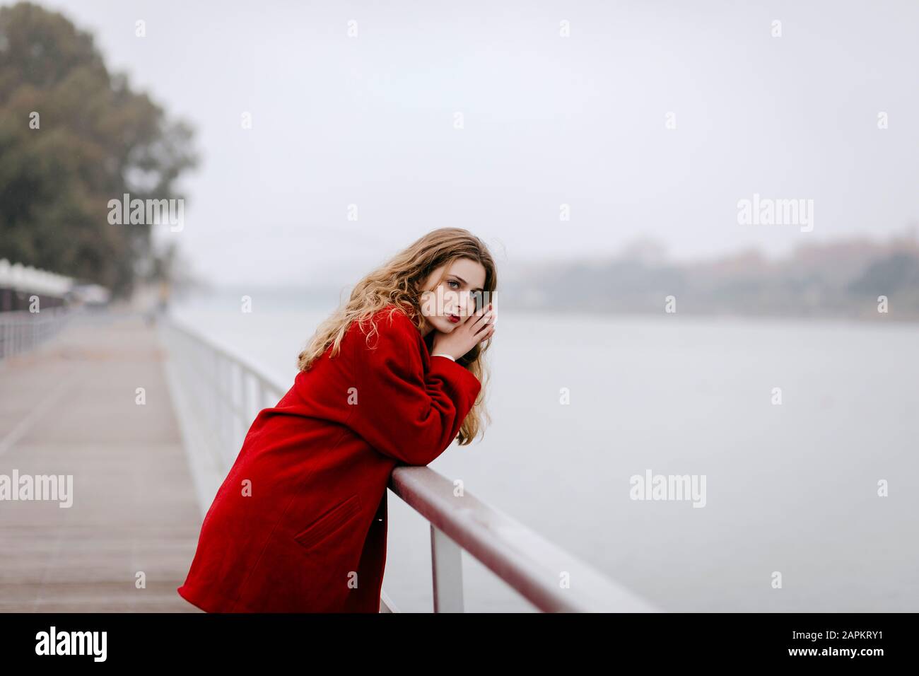 Portrait de la jeune femme portant un manteau rouge, se penchant sur la rampe le jour de la pluie Banque D'Images