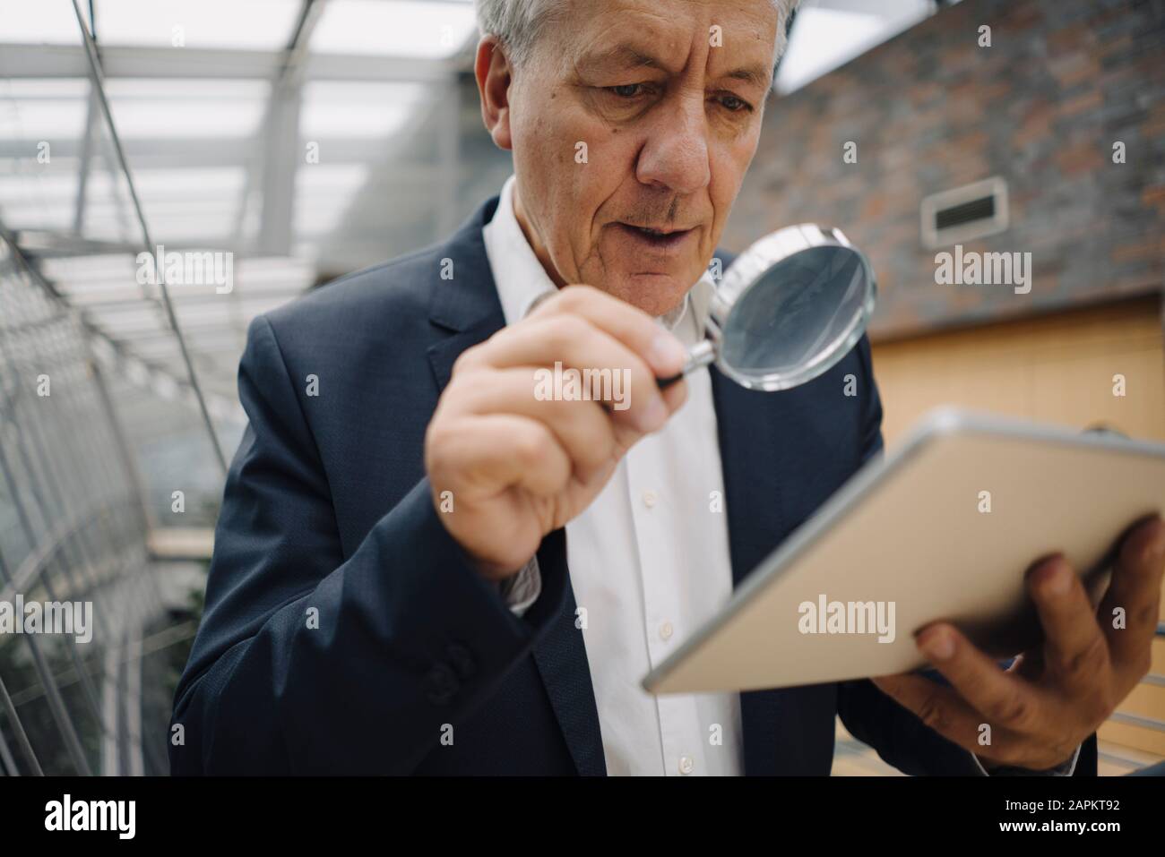 Homme d'affaires senior avec une tablette de lecture en loupe au bureau Banque D'Images