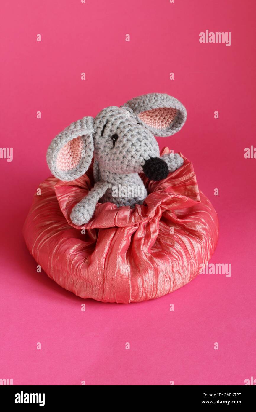 La souris en peluche tricotée grise se trouve dans un sac en soie rose sur fond de papier rose Banque D'Images