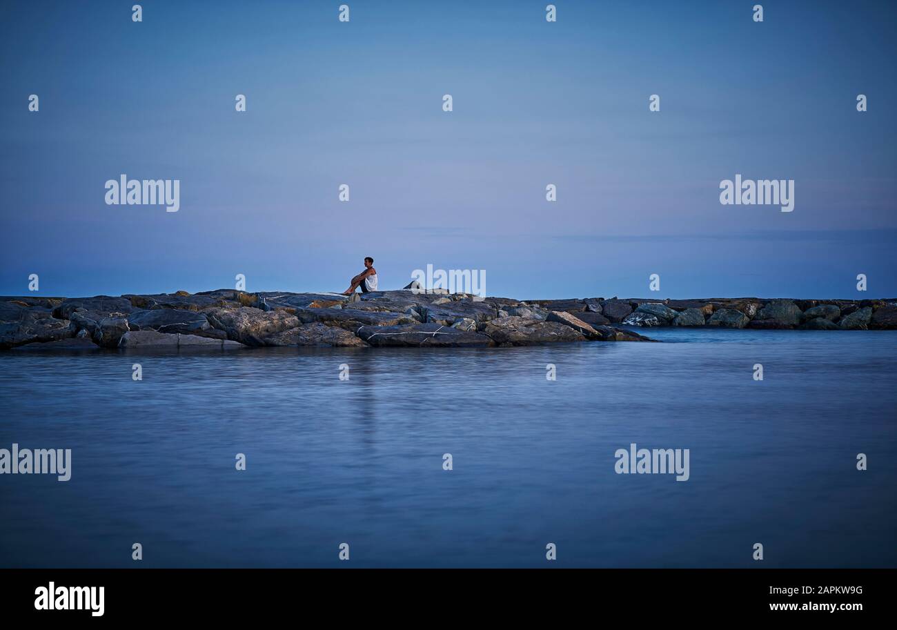 Femme mûre assise à l'entrée du port au crépuscule en regardant à distance, Italie Banque D'Images