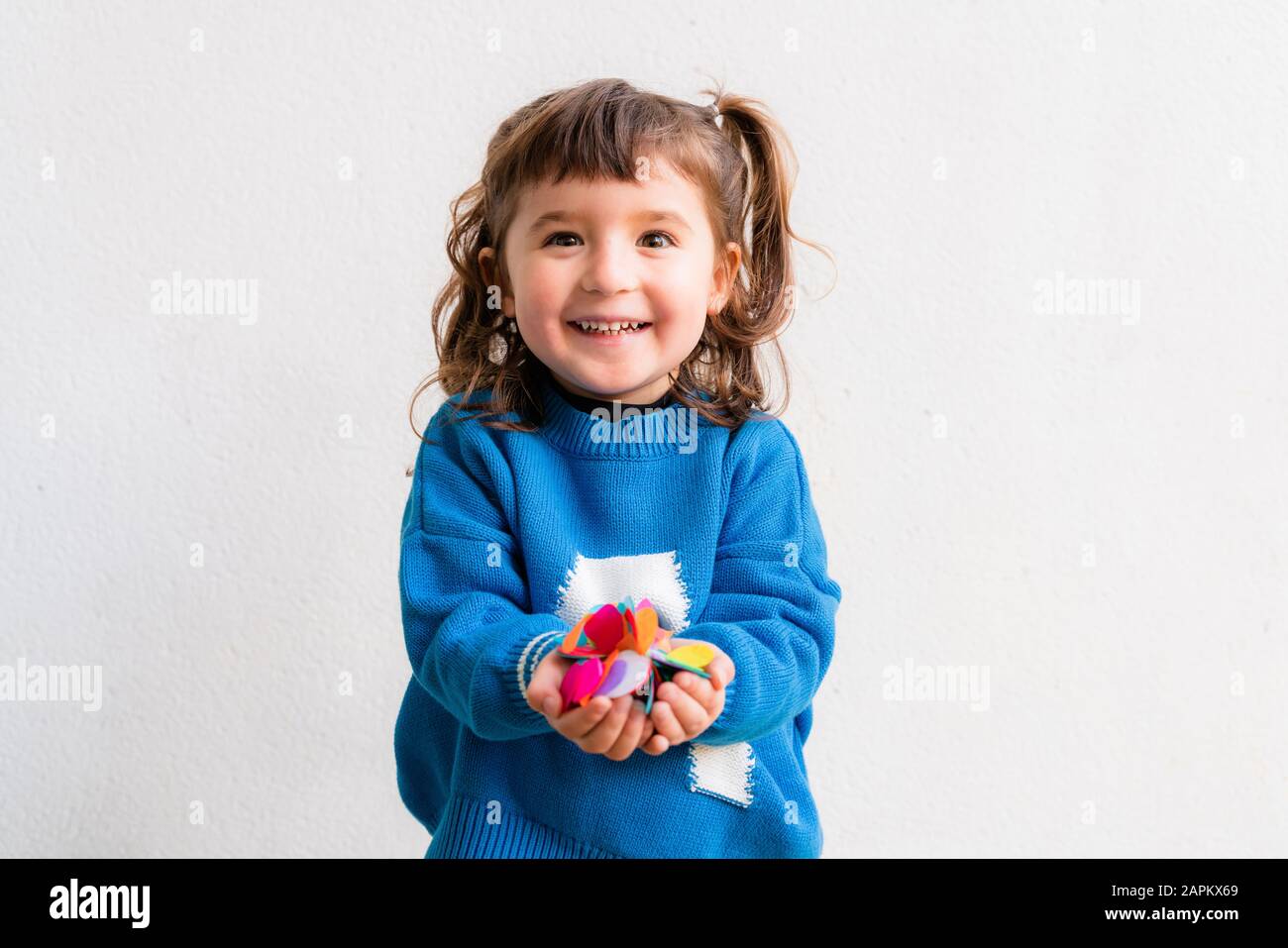 Bonne petite fille soufflant les confettis à une fête devant un mur blanc Banque D'Images