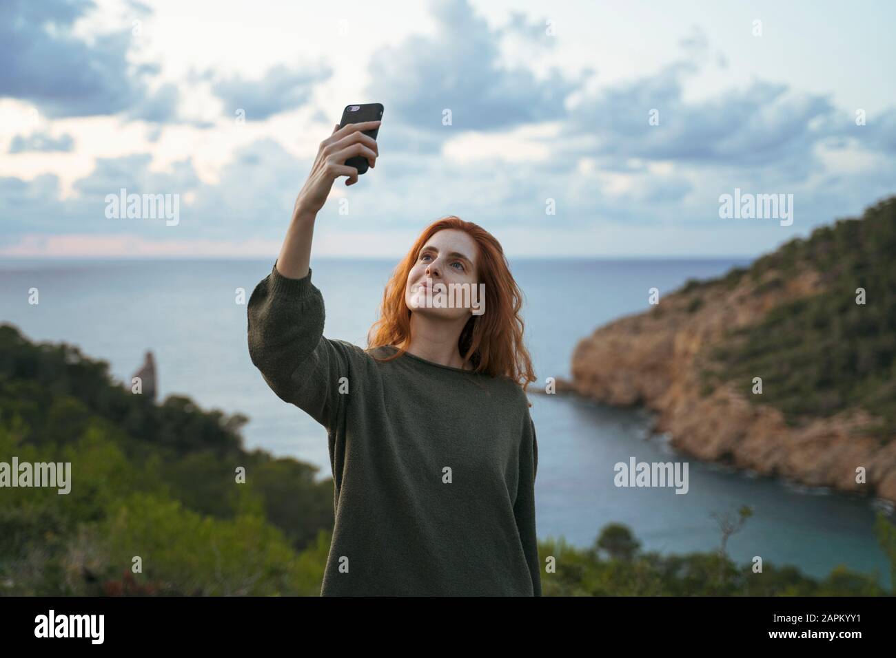 Jeune femme à tête rouge prenant un selfie sur la côte, Ibiza, Espagne Banque D'Images
