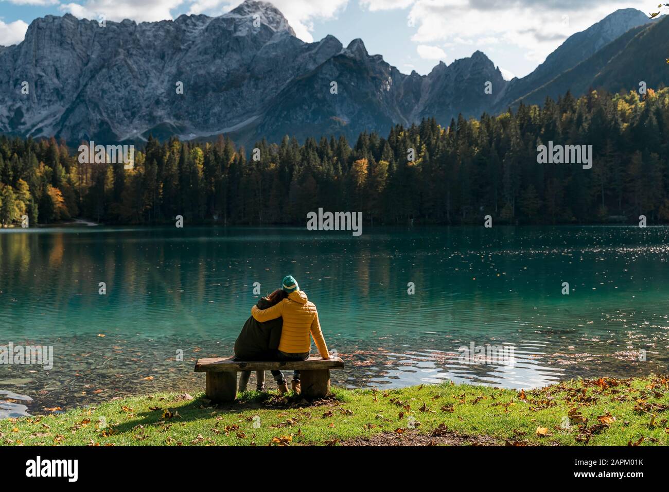 Vue arrière du couple assis sur un banc à Laghi di Fusine, Friuli Venezia Giulia, Italie Banque D'Images