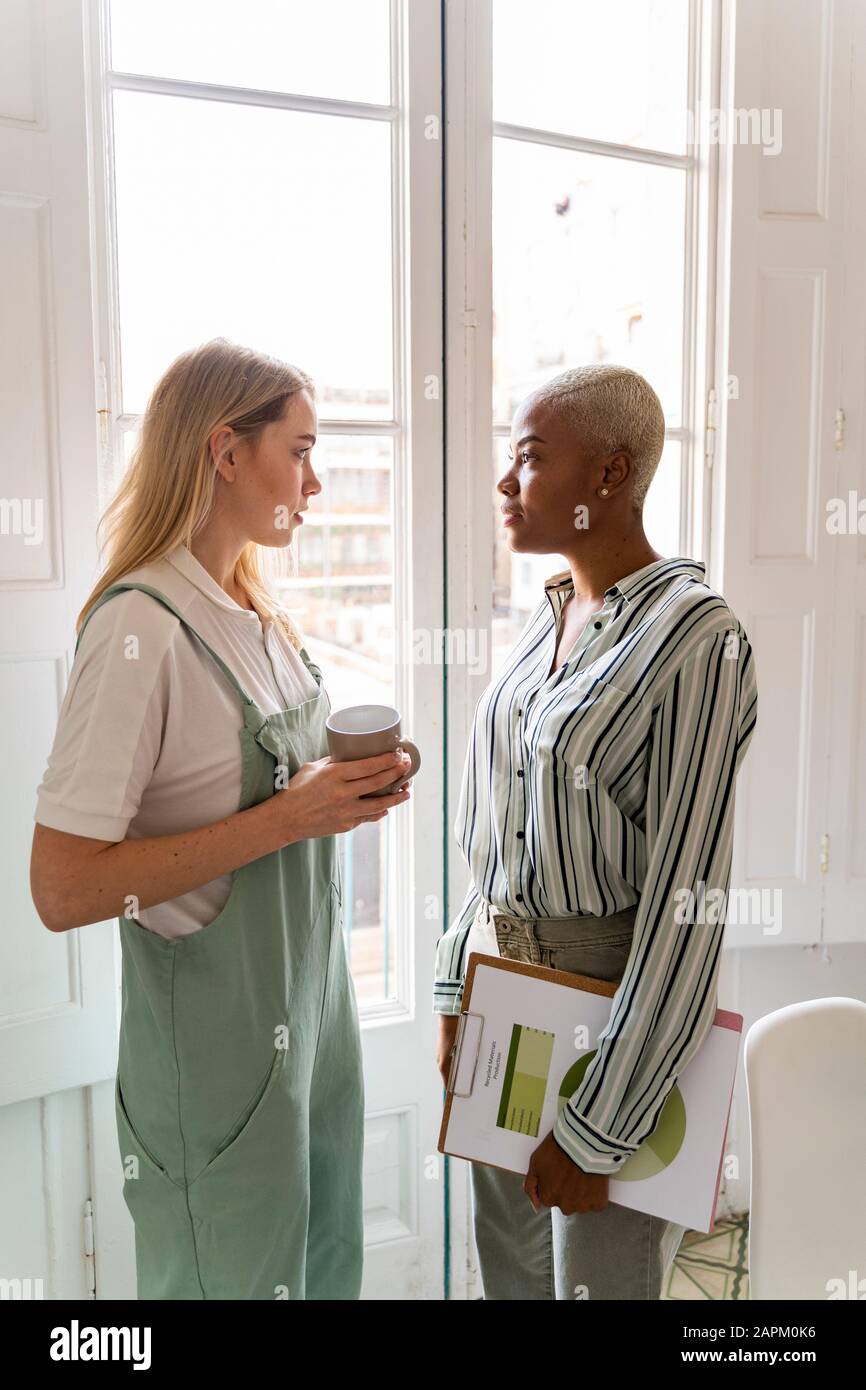 Deux femmes avec des documents et une tasse de café debout à la fenêtre Banque D'Images