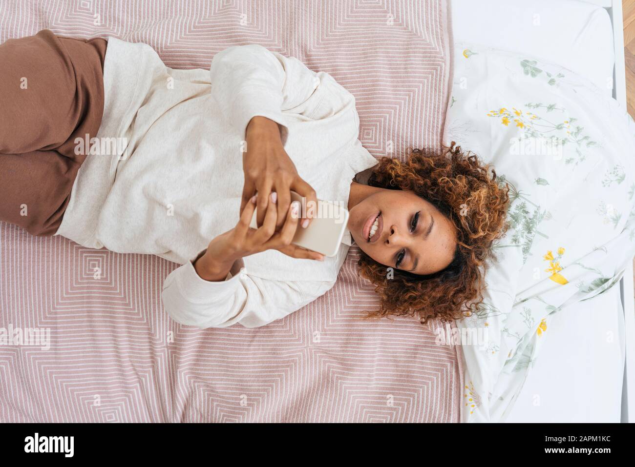 Jeune femme posée au lit à l'aide d'un smartphone Banque D'Images