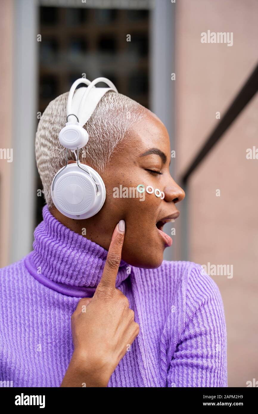 Portrait d'une femme aux cheveux blancs avec un casque blanc et des autocollants sur son visage pour écouter de la musique et rire Banque D'Images