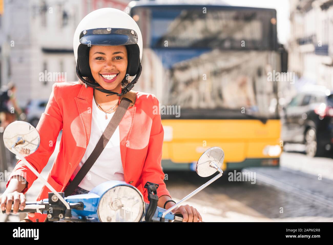 Portrait de heureuse jeune femme qui monte en scooter motorisé dans la ville, Lisbonne, Portugal Banque D'Images