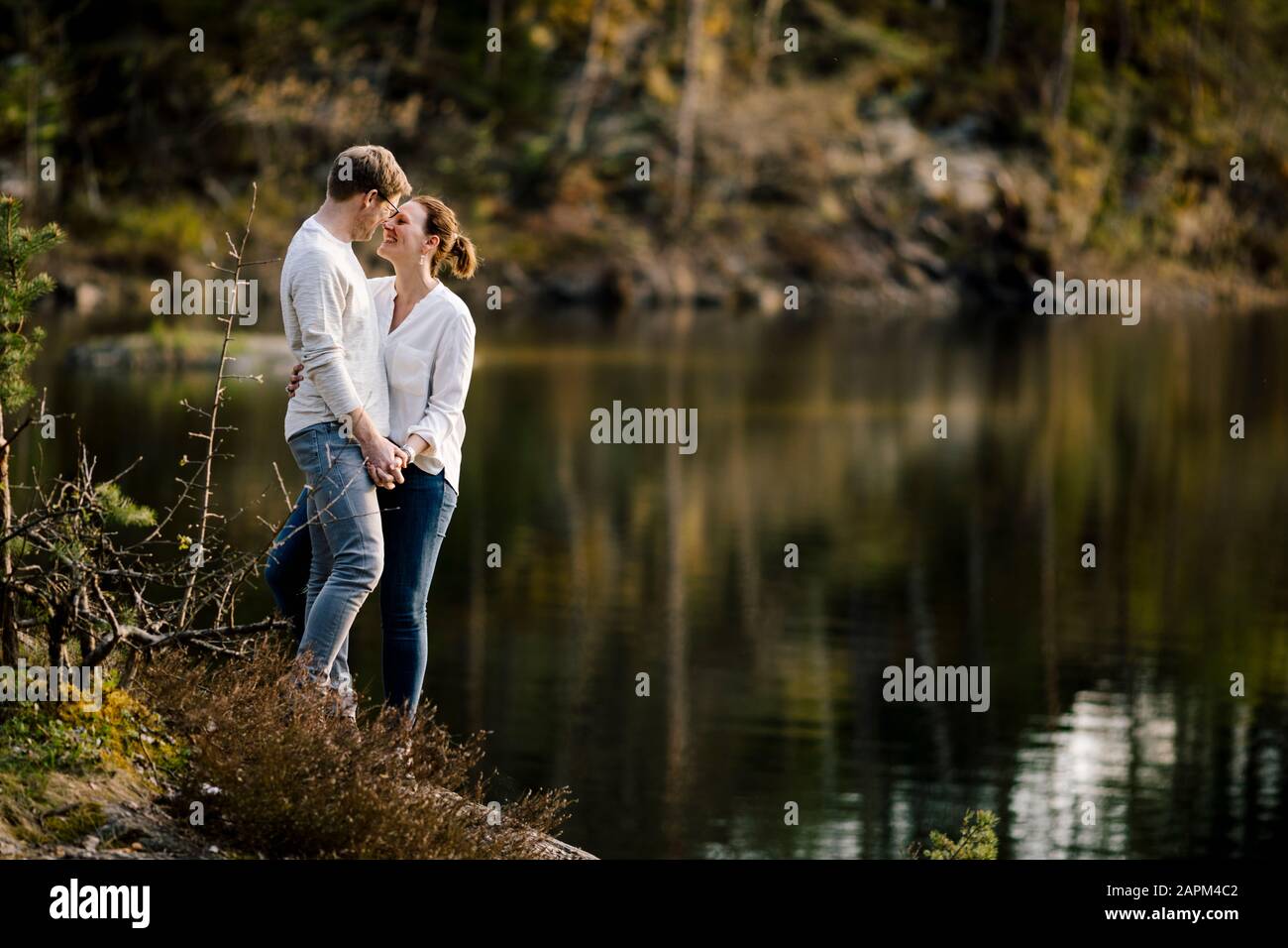 Couple affectueux debout sur un rocher au bord du lac, Forstsee, Carinthie, Autriche Banque D'Images