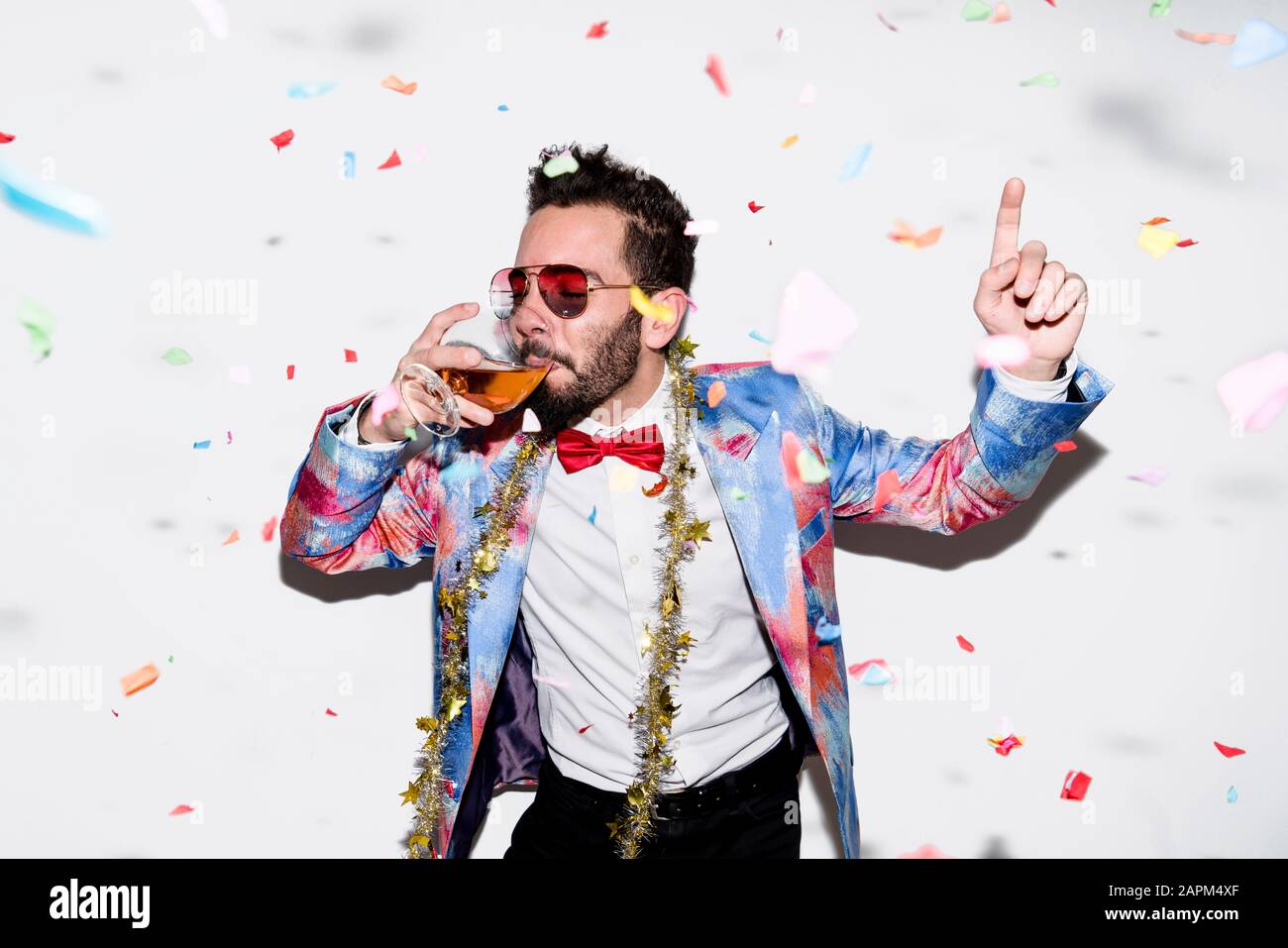 Un homme cool et élégant portant un costume coloré et des lunettes de soleil célébrant une fête avec des confettis et de la boisson Banque D'Images