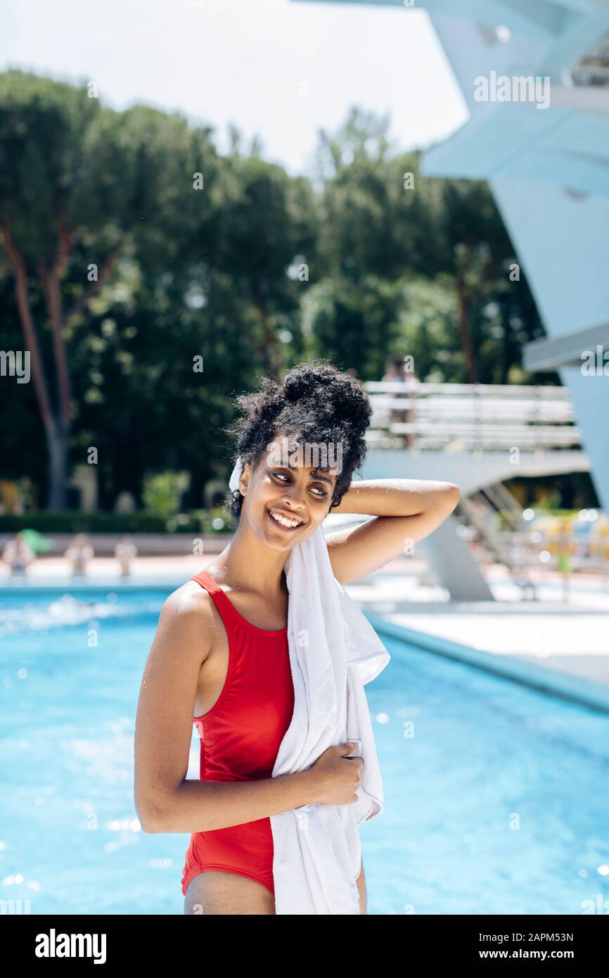 Portrait d'une jeune femme souriante dans une combinaison de bain rouge qui s'est remorchée devant une piscine Banque D'Images