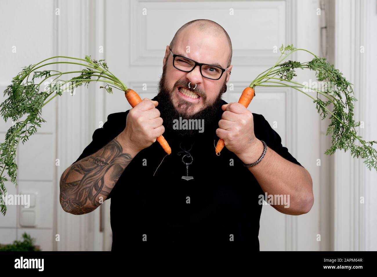 Portrait d'un homme barbu en colère tenant des carottes dans la cuisine Banque D'Images