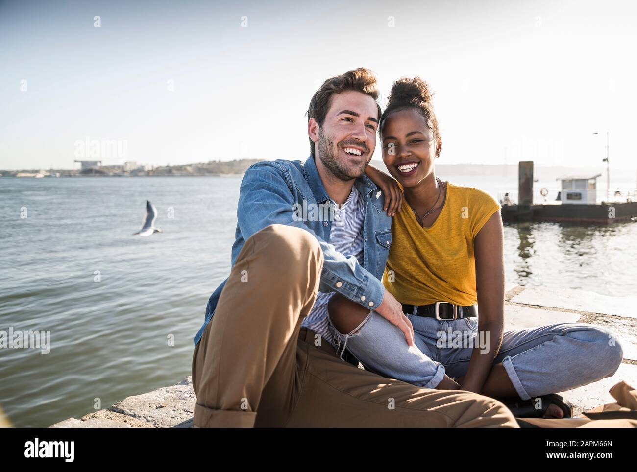 Happy young couple sitting on pier au Waterfront, Lisbonne, Portugal Banque D'Images