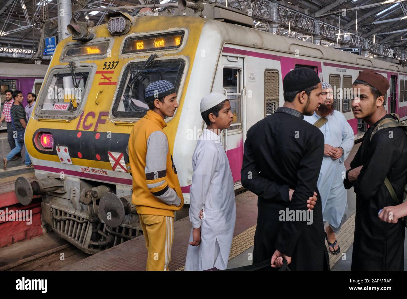 Un groupe d'hommes musulmans en tenue traditionnelle devant un moteur de train à Chhatrapati Shivaji Maharaj Terminus (CSMT) à Mumbai, en Inde Banque D'Images