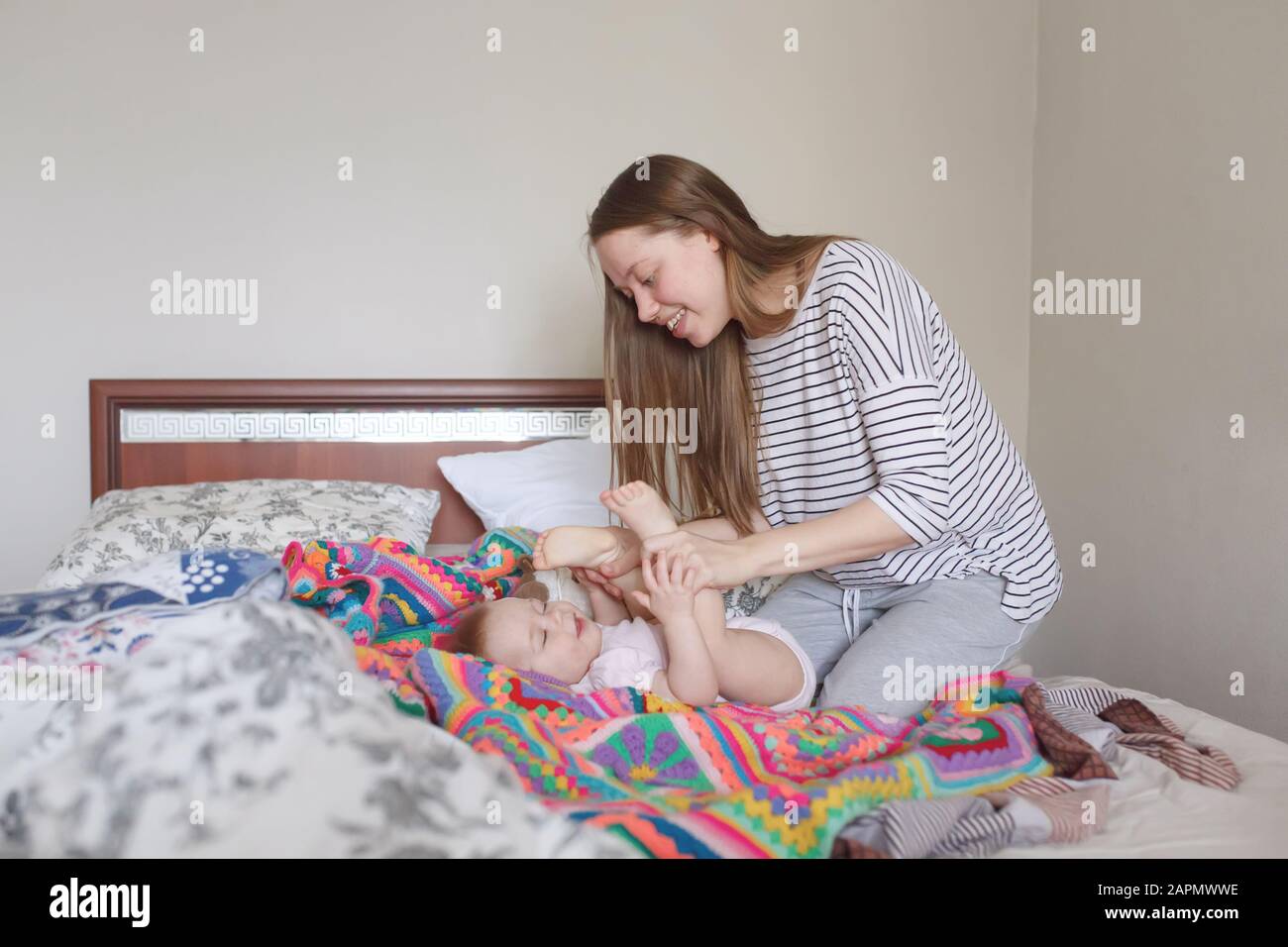 Jeune belle mère prenant soin de son petit bébé mignon le matin dans la  chambre à coucher, pleine hauteur, vue latérale Photo Stock - Alamy