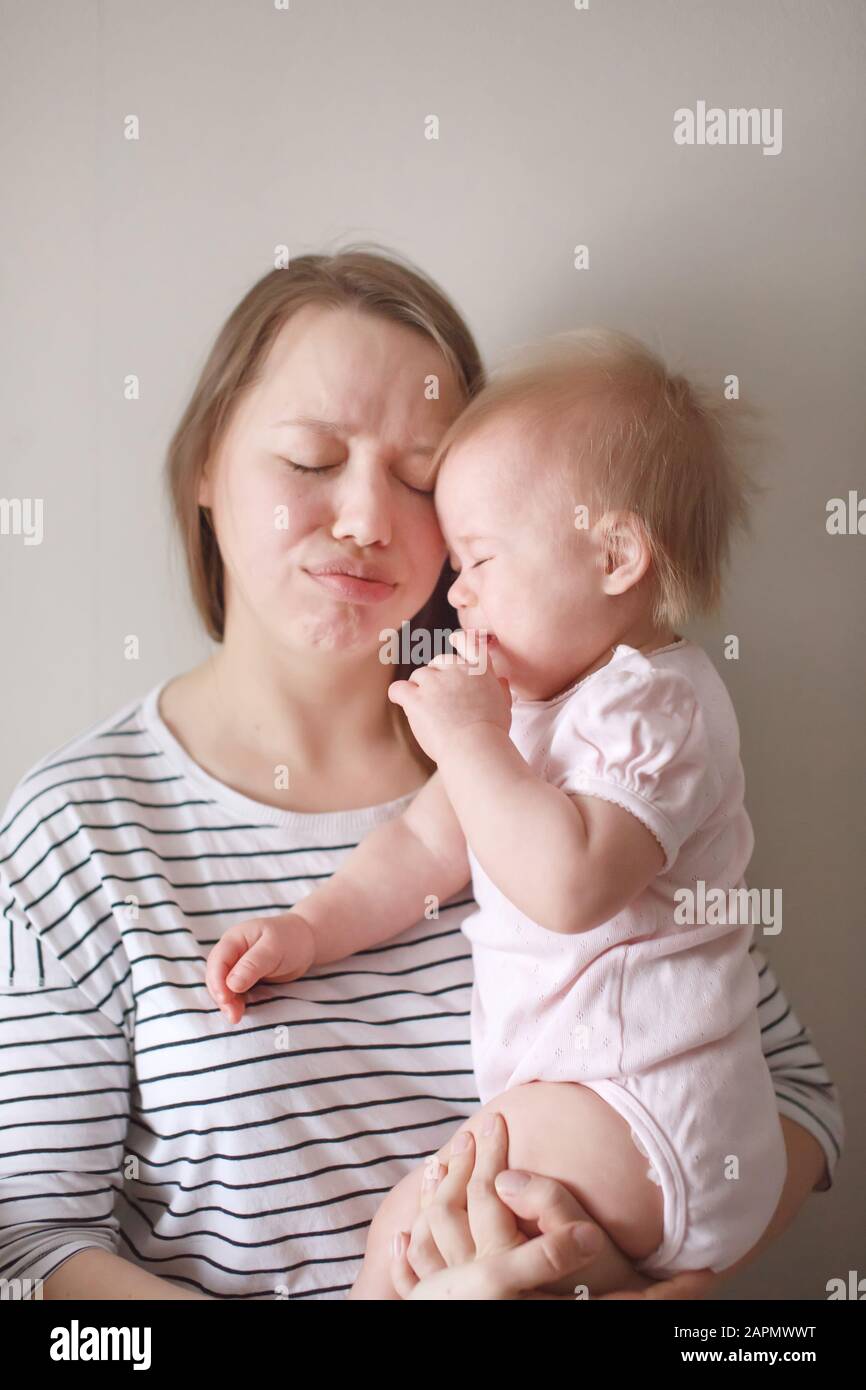Jeune belle mère tenant son petit bébé pleurant sur ses mains et faisant la grimace drôle sur le visage Banque D'Images