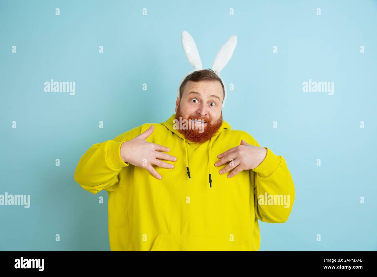 Se pointant sur lui-même. Homme caucasien comme lapin de Pâques avec des vêtements décontractés lumineux sur fond bleu studio. Joyeuses salutations de pâques. Concept d'émotions humaines, d'expression faciale, de vacances. Copyspace. Banque D'Images