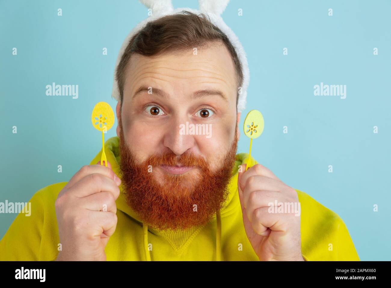 Homme caucasien au décor traditionnel comme lapin de Pâques avec des vêtements clairs et décontractés sur fond de studio bleu. Joyeuses salutations de pâques. Concept d'émotions humaines, d'expression faciale, de vacances. Copyspace. Banque D'Images