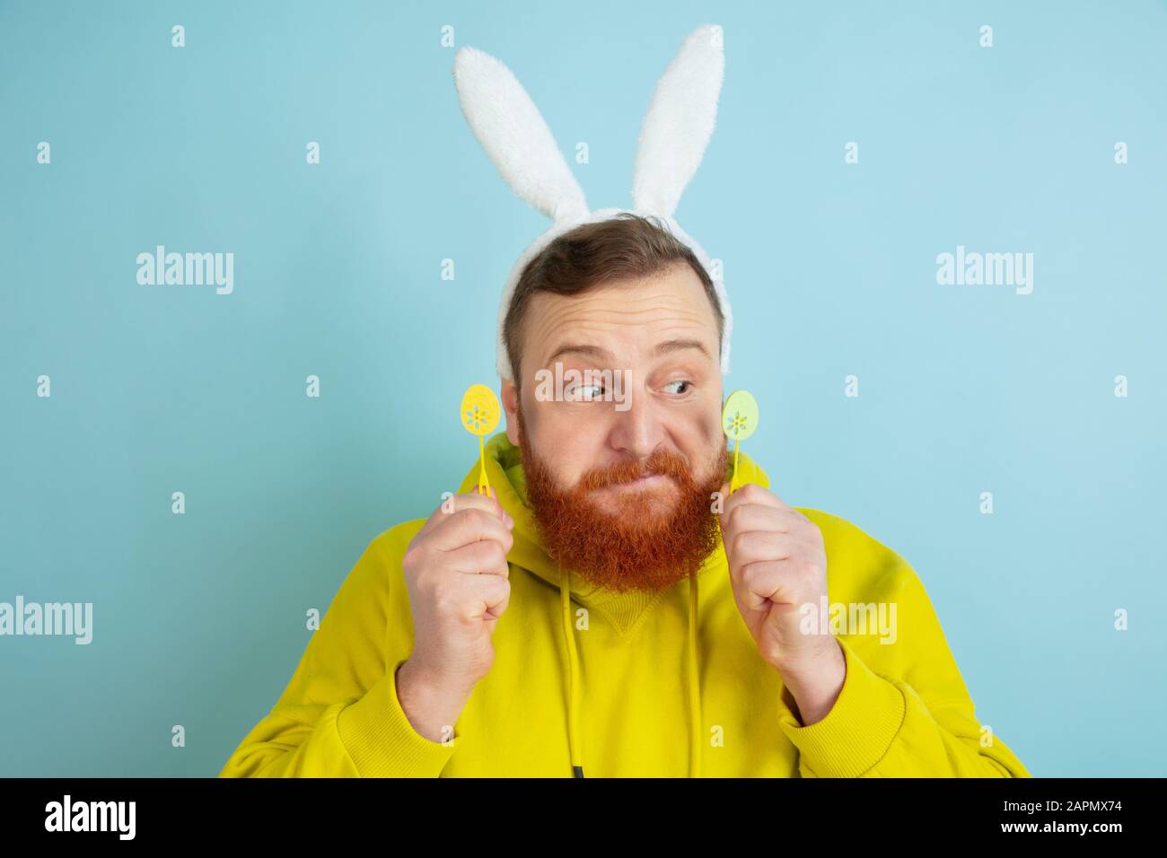 Homme caucasien au décor traditionnel comme lapin de Pâques avec des vêtements clairs et décontractés sur fond de studio bleu. Joyeuses salutations de pâques. Concept d'émotions humaines, d'expression faciale, de vacances. Copyspace. Banque D'Images