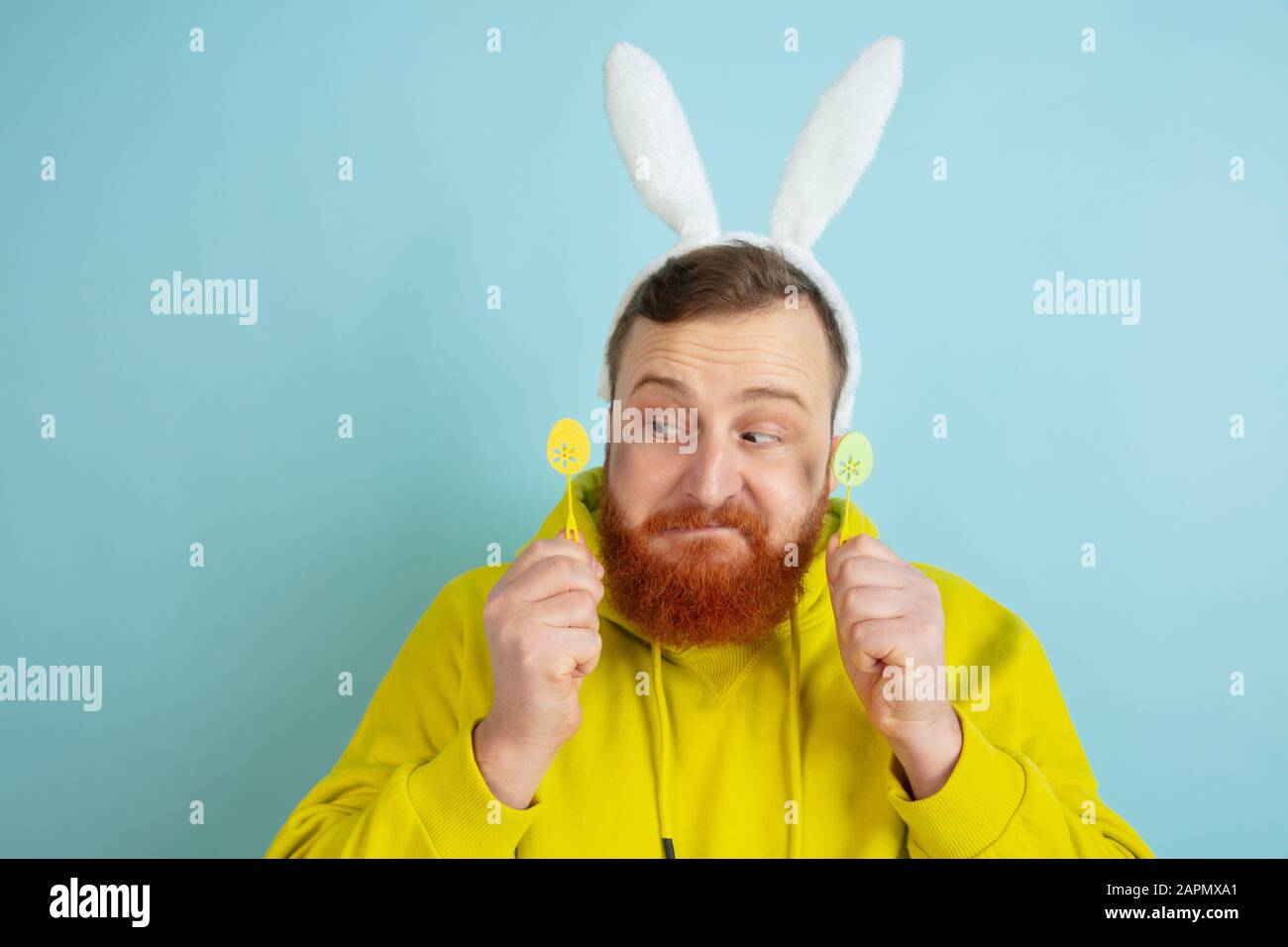 Homme caucasien au décor traditionnel comme lapin de Pâques avec des vêtements clairs et décontractés sur fond de studio bleu. Joyeuses salutations de pâques. Concept d'émotions humaines, d'expression faciale, de vacances. Copyspace. Banque D'Images